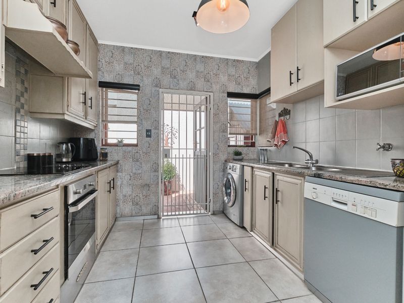 A functional kitchen featuring built-in cabinetry, granite countertops, integrated appliances, and tiled flooring, with direct access to an outdoor area via a security gate.