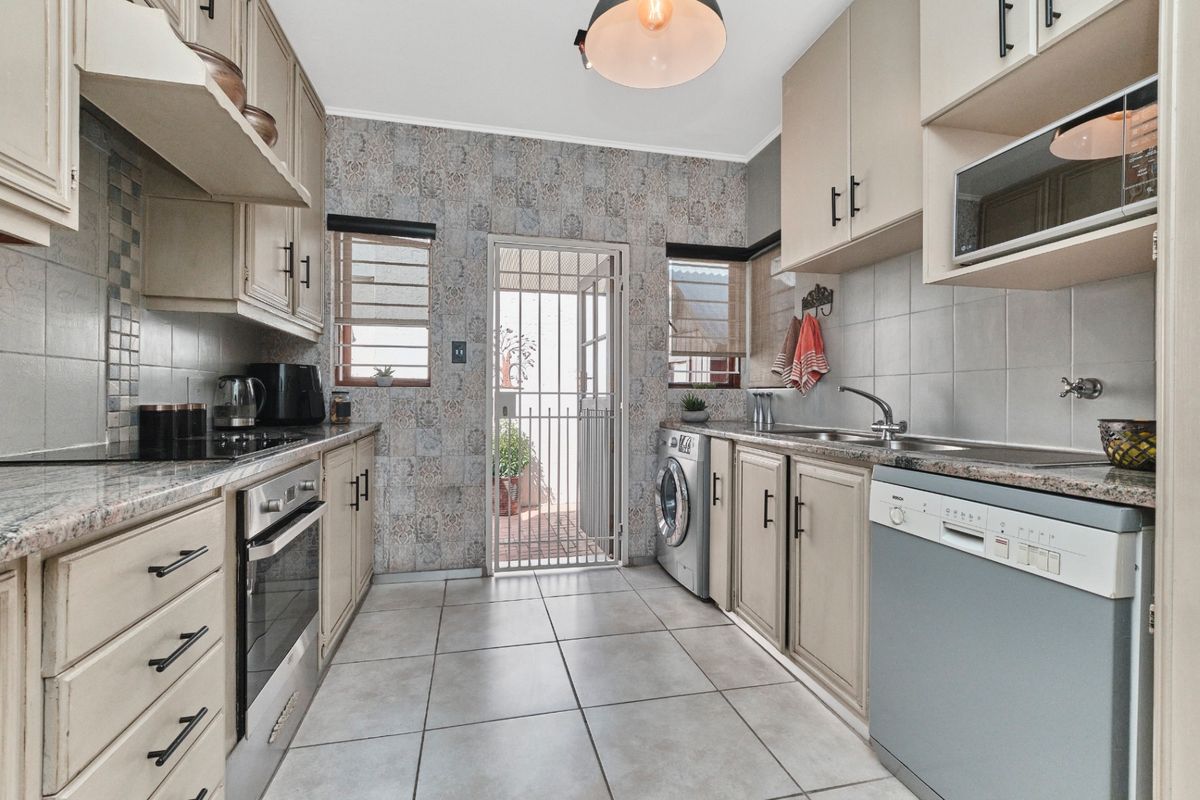 A functional kitchen featuring built-in cabinetry, granite countertops, integrated appliances, and tiled flooring, with direct access to an outdoor area via a security gate.