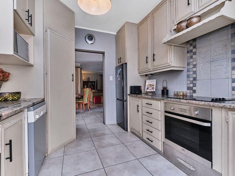 A functional kitchen featuring built-in cabinetry, granite countertops, an integrated oven and hob, and tiled flooring, with a direct view into the adjacent living area.