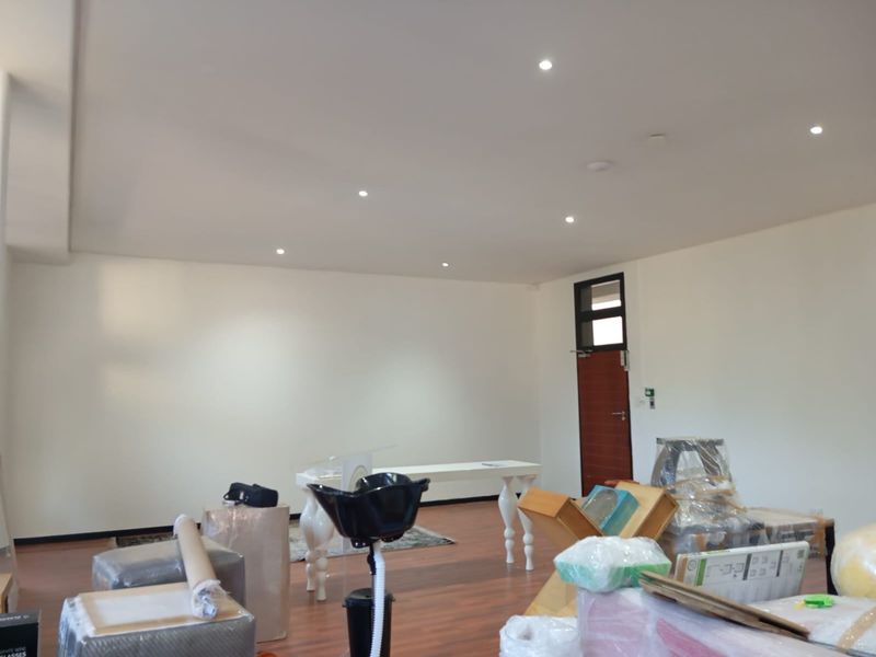 A spacious commercial interior featuring recessed downlighting, laminate flooring, and a single access door, currently used as a storage or workspace area.