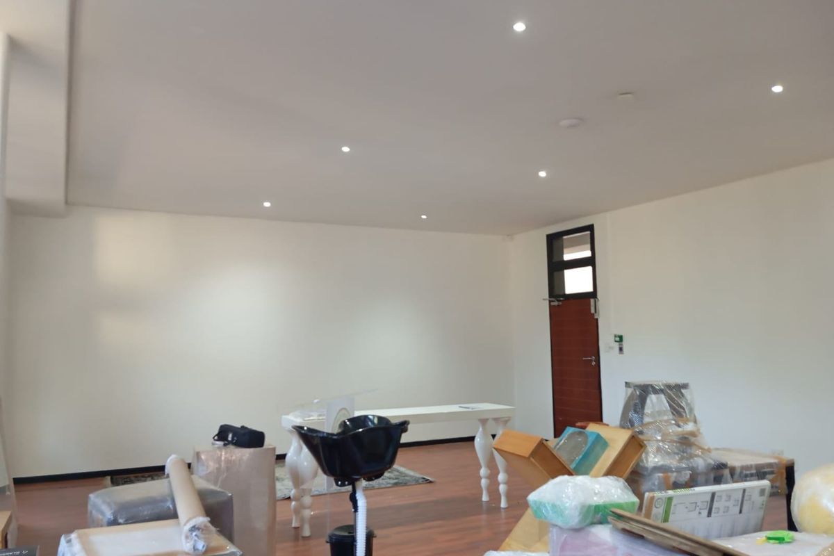 A spacious commercial interior featuring recessed downlighting, laminate flooring, and a single access door, currently used as a storage or workspace area.