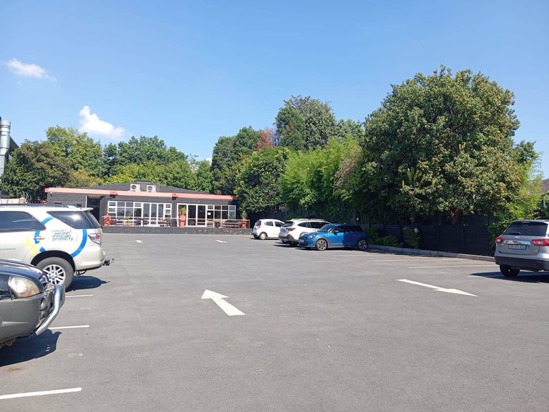 A commercial property featuring a paved parking area with marked bays and a building facade with large glass windows and external air conditioning units.