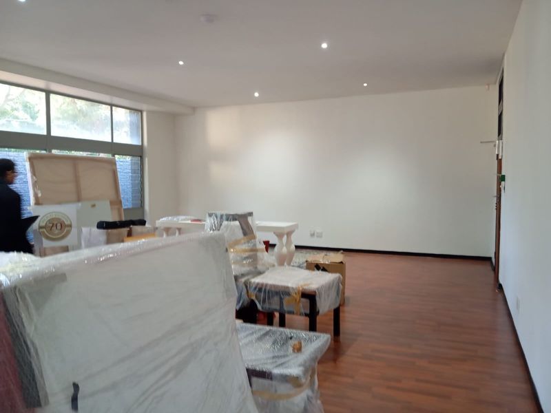 A spacious, well-lit living area featuring laminate flooring and large windows, currently being used for storage.