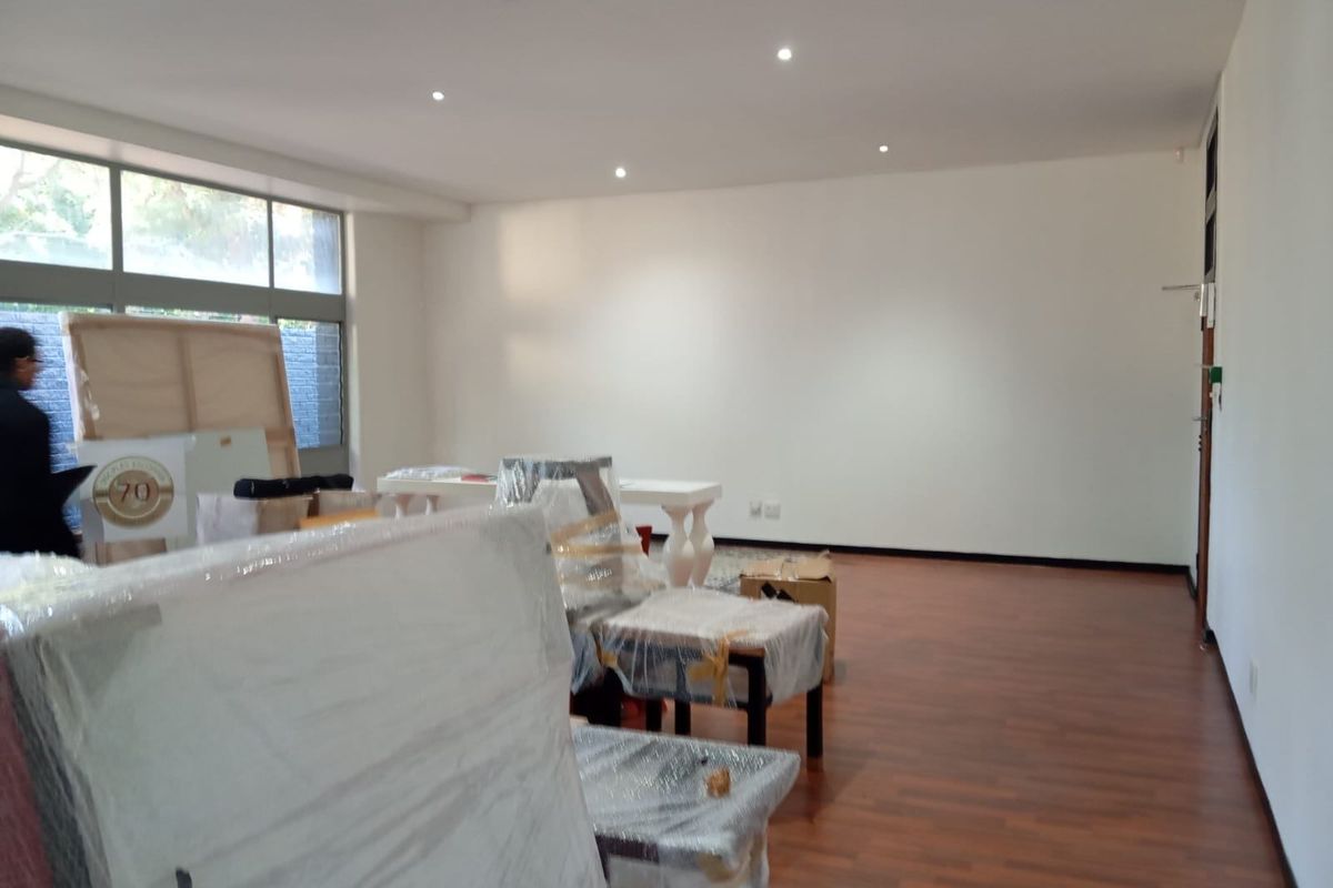 A spacious, well-lit living area featuring laminate flooring and large windows, currently being used for storage.