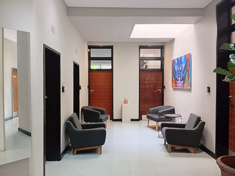 A bright and modern commercial hallway featuring tiled flooring, a large skylight, and multiple access doors, providing a clean and professional reception or waiting area.