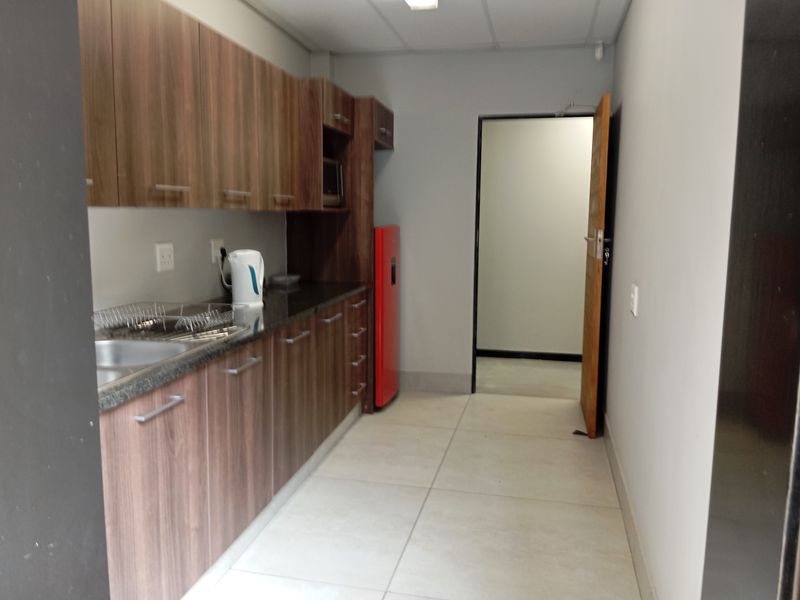 A clean, functional kitchenette featuring wood-finish cabinetry, granite countertops, and large format floor tiles, suitable for office or commercial use.