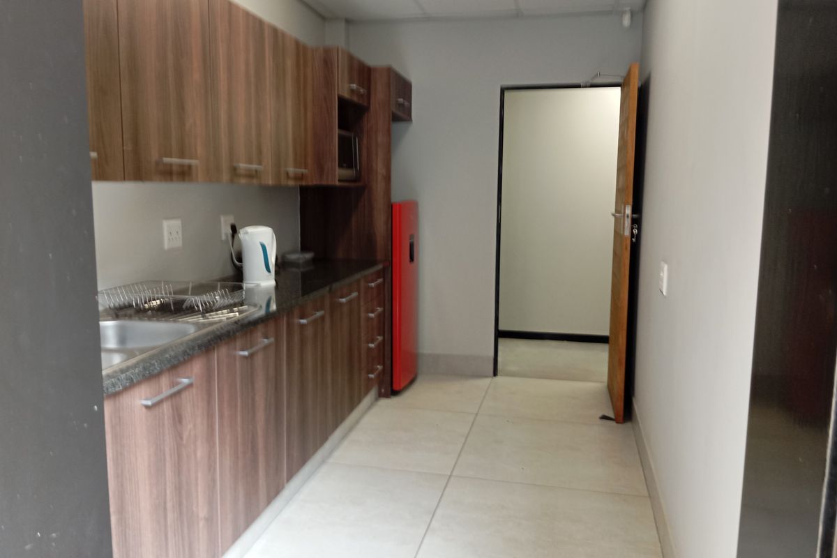 A clean, functional kitchenette featuring wood-finish cabinetry, granite countertops, and large format floor tiles, suitable for office or commercial use.
