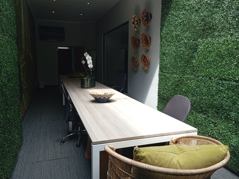 A modern commercial office space featuring a long built-in desk, recessed ceiling lighting, and decorative artificial grass wall cladding.