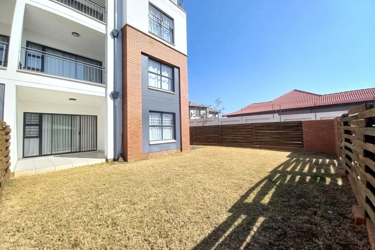 Rear view of an apartment building featuring a private garden, timber fencing, and a ground-floor patio with sliding door access.