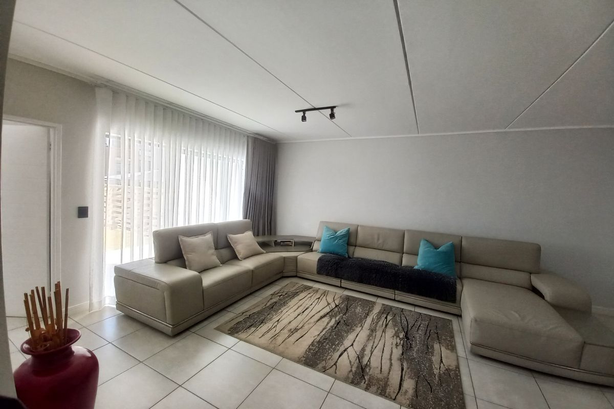 A spacious living room featuring neutral tiled flooring, modern track lighting, and large sliding doors with vertical blinds for natural light.