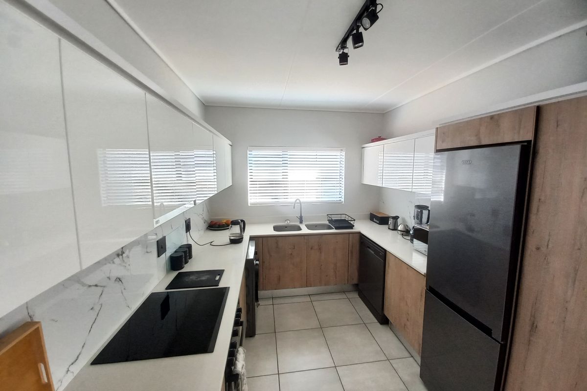 Modern galley-style kitchen featuring high-gloss white cabinetry, wood-grain lower cupboards, stone countertops, integrated hob, and tiled flooring.