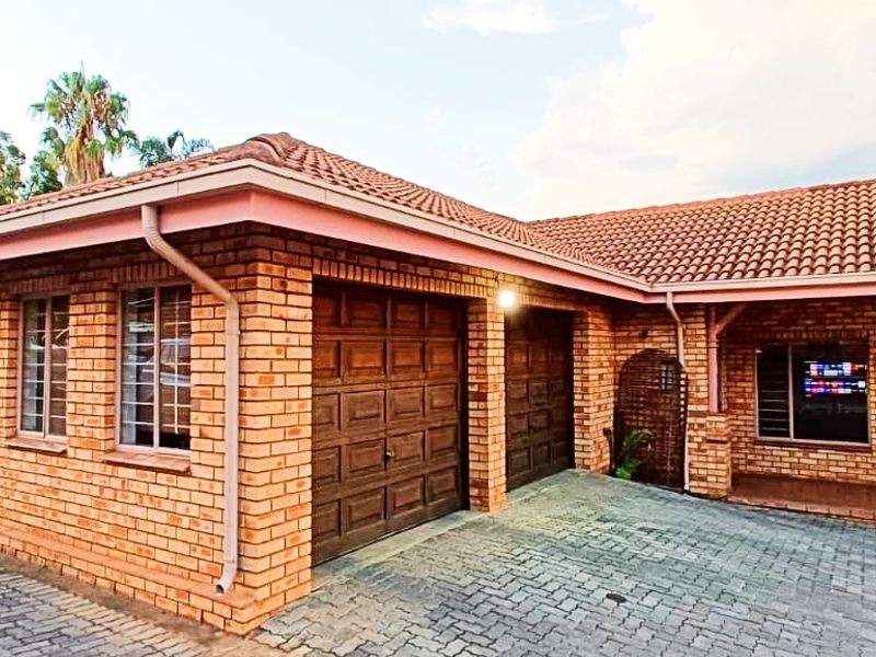 Front view of a brick townhouse featuring a double garage, tiled roof, and paved driveway area.