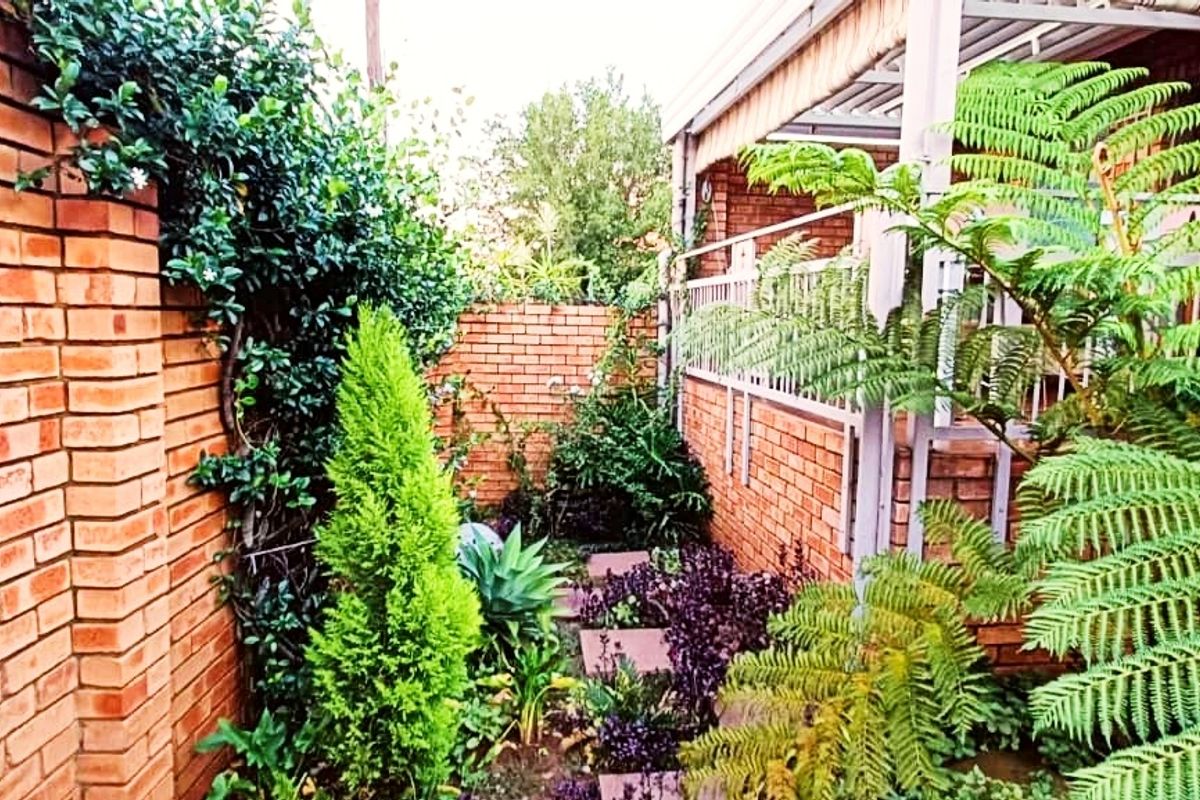 A private rear garden area featuring face brick walls, a paved walkway, and a covered patio with metal railings.