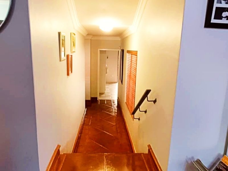A view looking down a hallway with tiled flooring, crown molding, and a wall-mounted handrail leading towards an adjacent room.