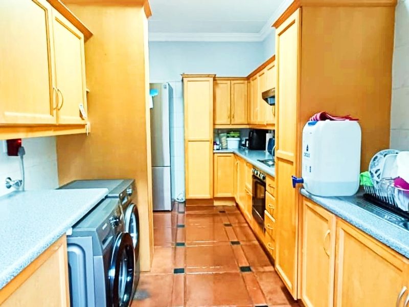 A functional kitchen featuring wooden cabinetry, laminate countertops, built-in oven, extractor fan, and tiled flooring.