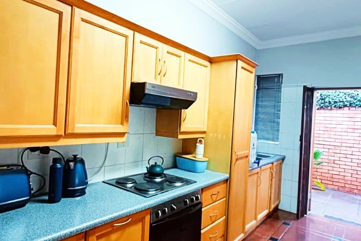 A functional kitchen featuring wooden cabinetry, laminate countertops, built-in oven with hob, and direct access to an outdoor courtyard area.