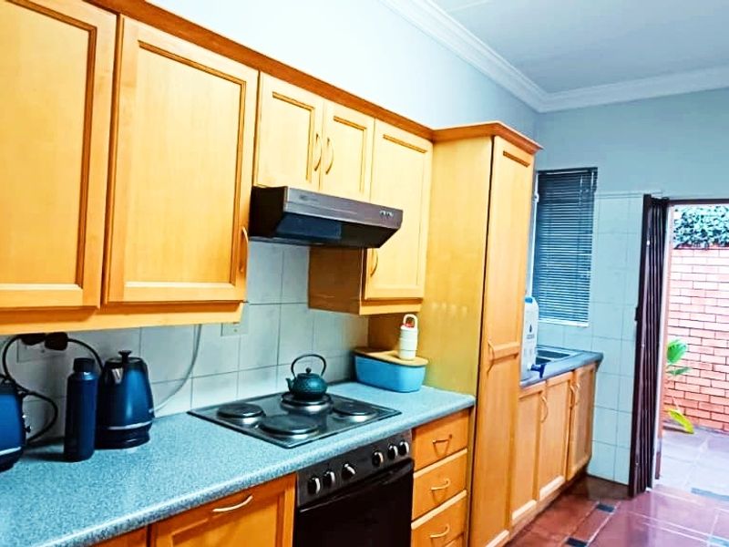 A functional kitchen featuring wooden cabinetry, laminate countertops, built-in oven with hob, and direct access to an outdoor courtyard area.