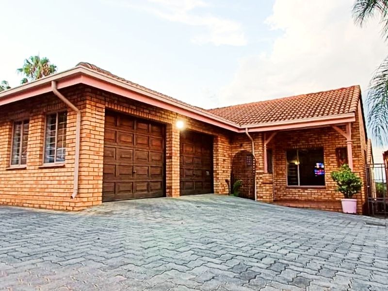 Front view of a brick townhouse featuring a double garage, tiled roof, and a paved driveway.
