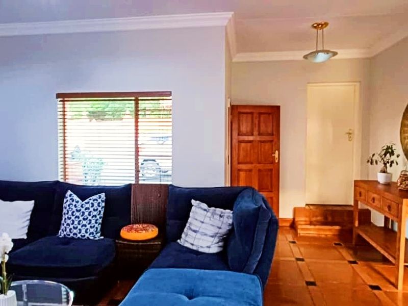 A comfortable living room featuring polished timber flooring, coved ceilings, and natural light through venetian blinds, leading to an internal doorway.
