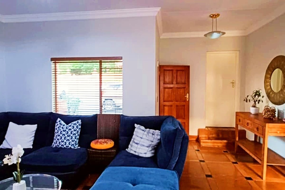 A comfortable living room featuring polished timber flooring, coved ceilings, and natural light through venetian blinds, leading to an internal doorway.