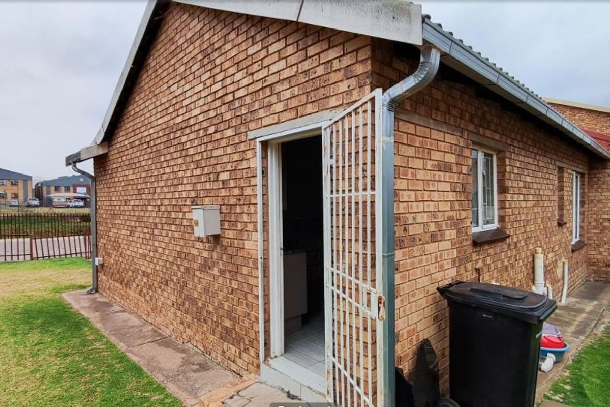Rear exterior view of the townhouse featuring face brick construction, security gate access, and functional guttering system.