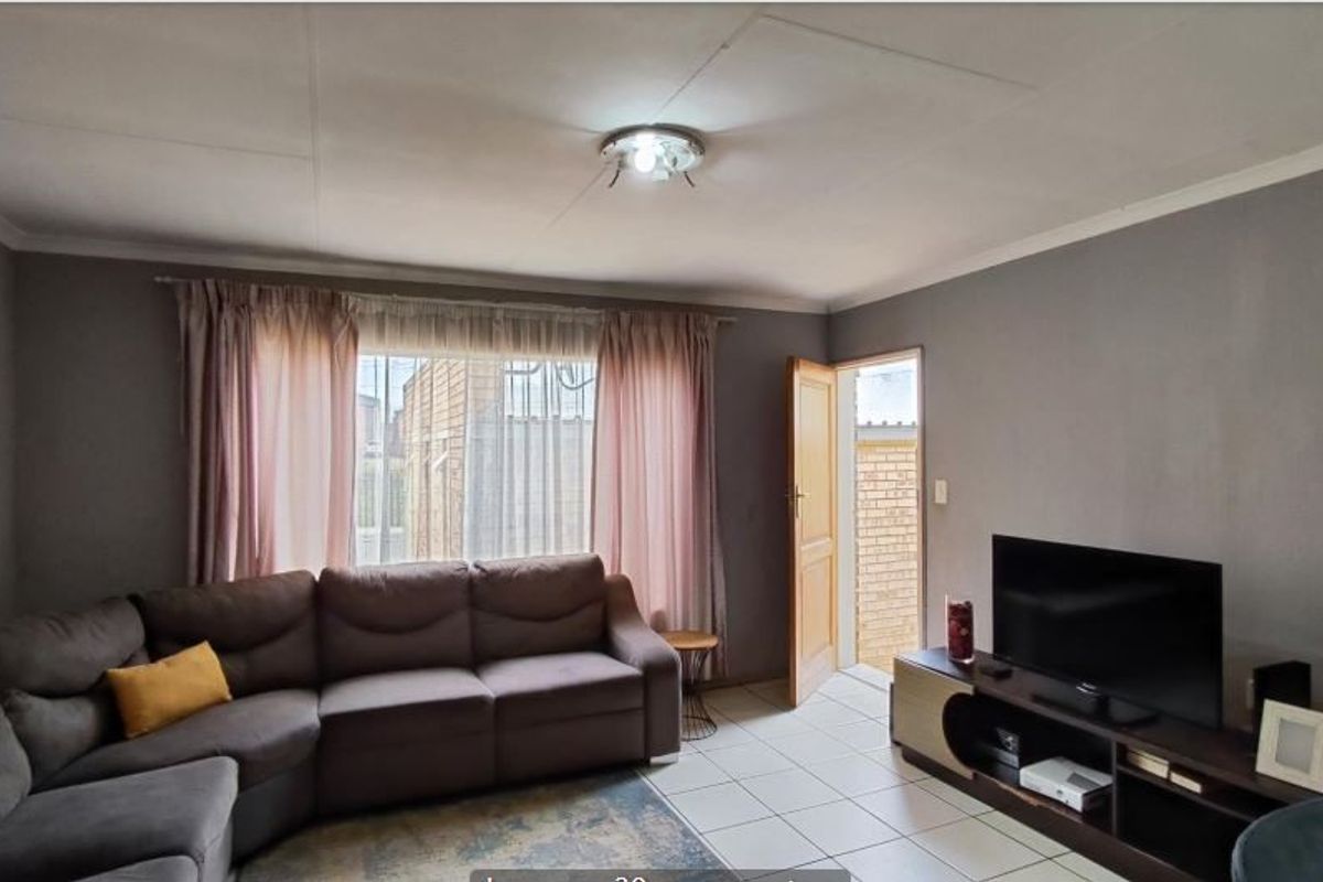 A functional living room featuring tiled flooring, coved ceilings, and a window with security bars, providing direct access to the exterior.