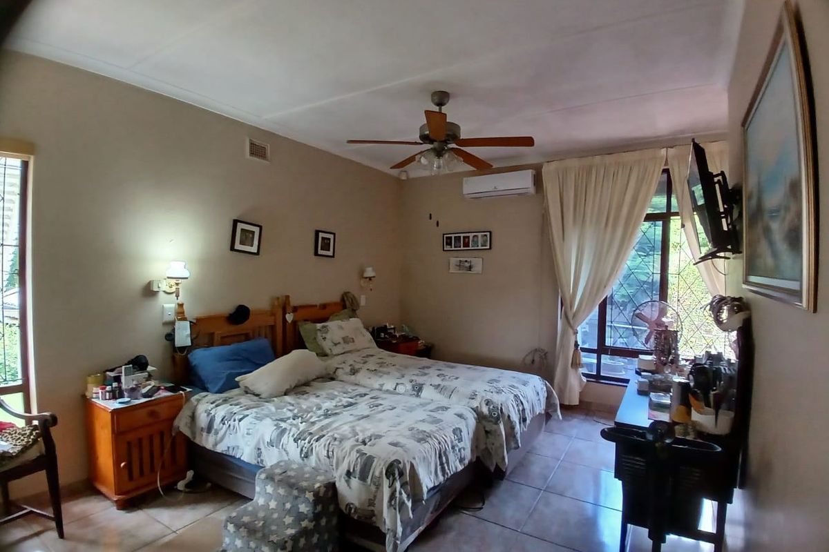 A functional bedroom featuring tiled flooring, a ceiling fan, and a wall-mounted air conditioning unit.