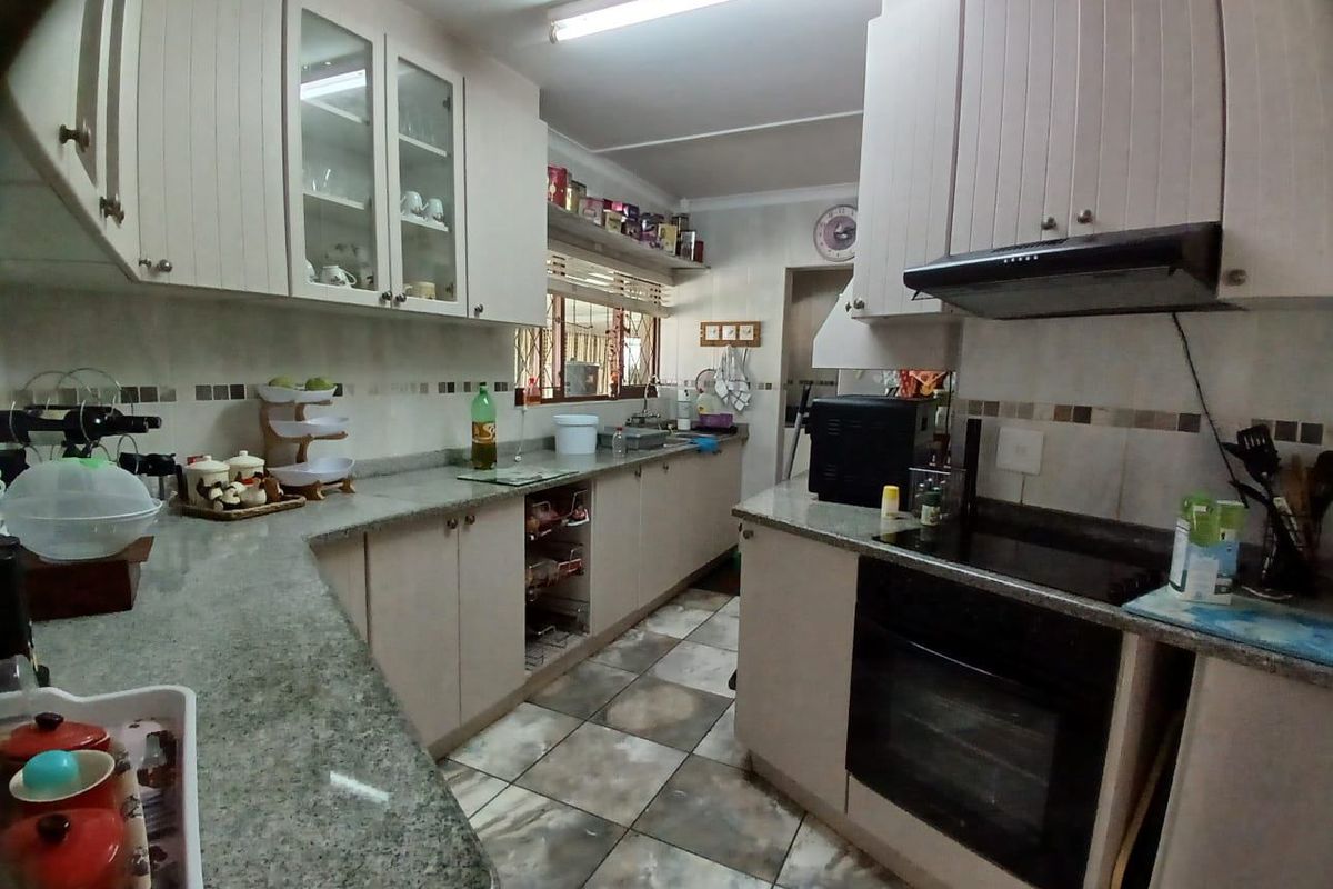 A functional kitchen featuring granite countertops, built-in oven, electric hob, extractor fan, and ample cabinetry with a tiled backsplash and flooring.