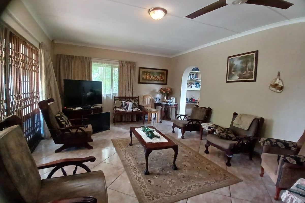 A spacious living room featuring tiled flooring, a ceiling fan, and an arched entryway leading to a built-in shelving nook.