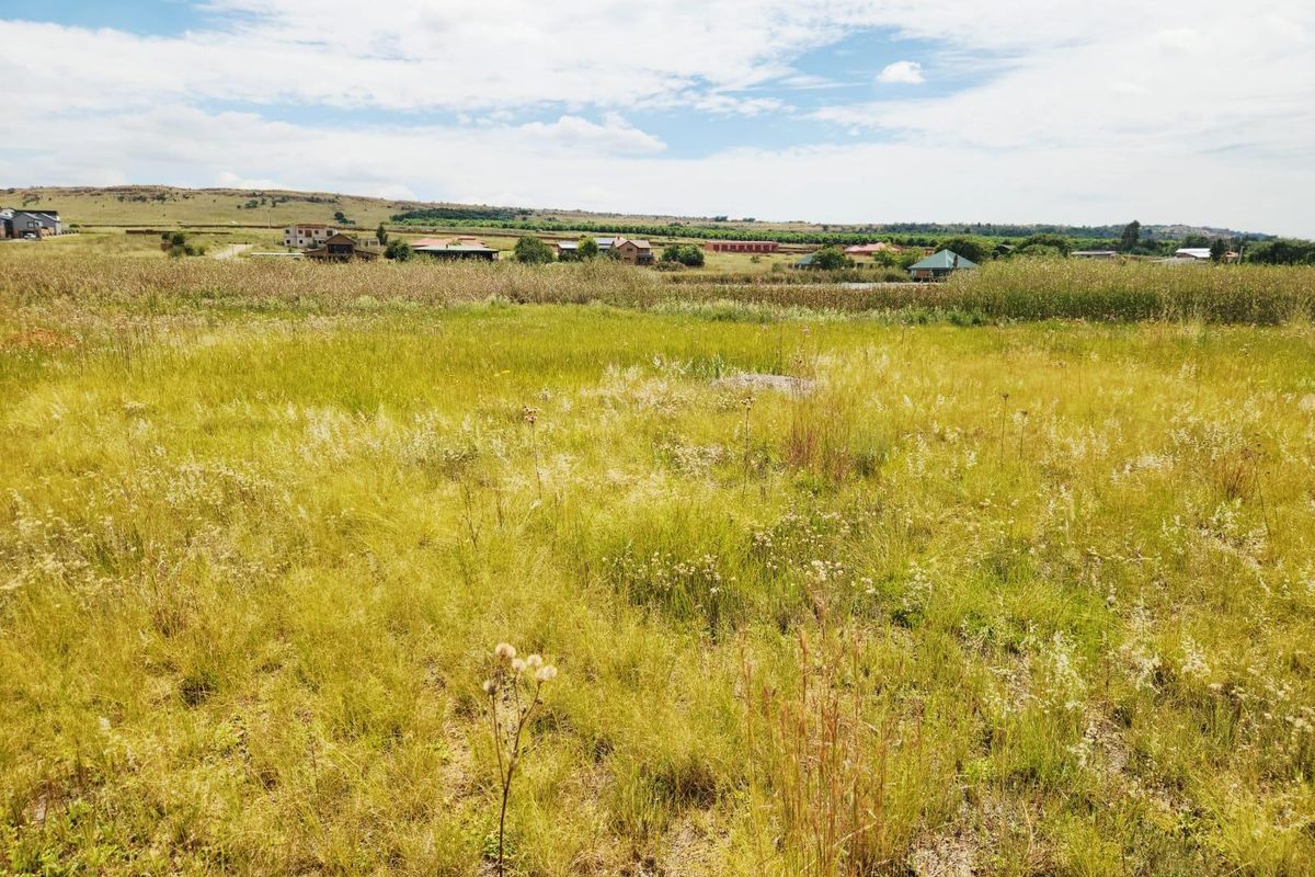 A wide-angle view of a vacant residential plot featuring natural grassland and surrounding rural landscape views.