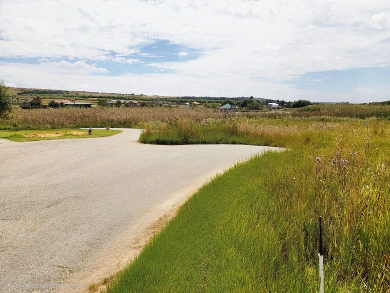 A view of a vacant residential plot featuring a paved access road and surrounding natural grassland landscape.