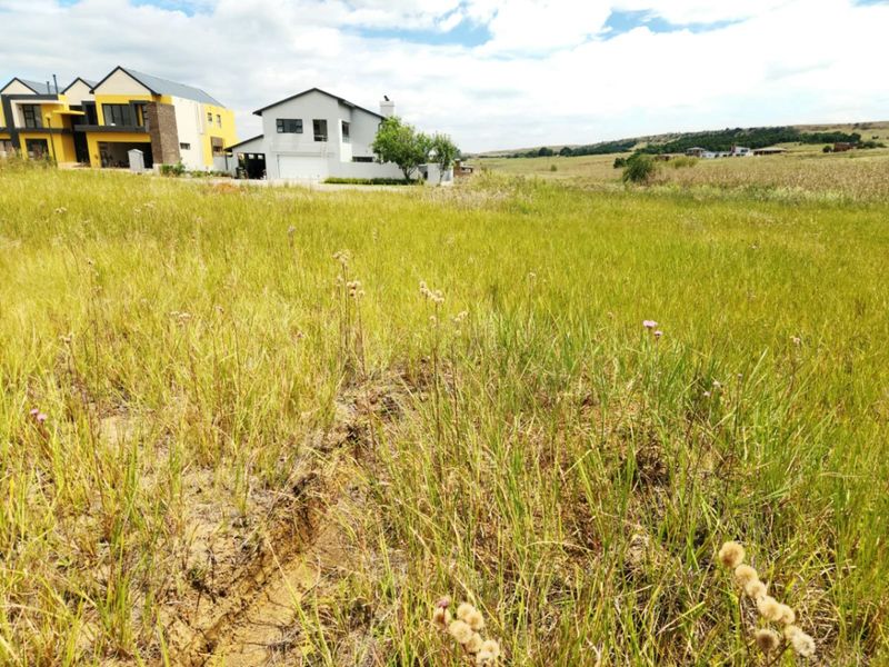 A view of a vacant residential plot featuring natural grassland with neighboring modern homes visible in the background.