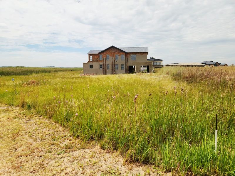 A view of a large residential property under construction, situated on a spacious, undeveloped plot of land with tall grass.