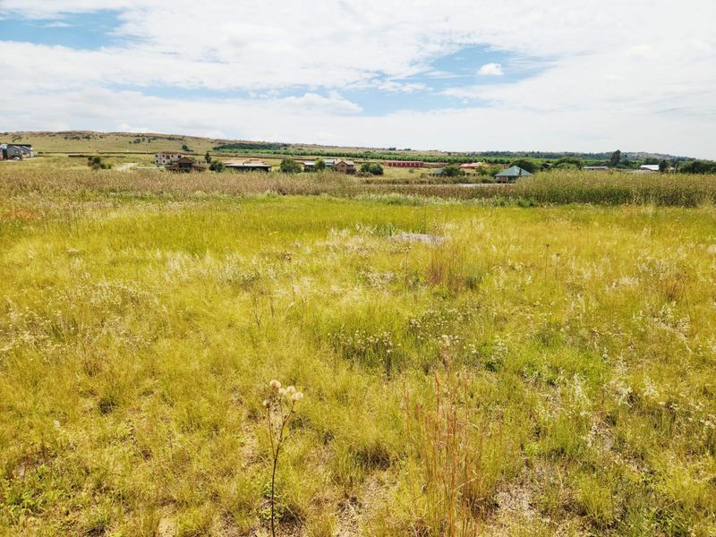 A wide-angle view of a vacant residential plot featuring natural grassland and surrounding rural landscape views.