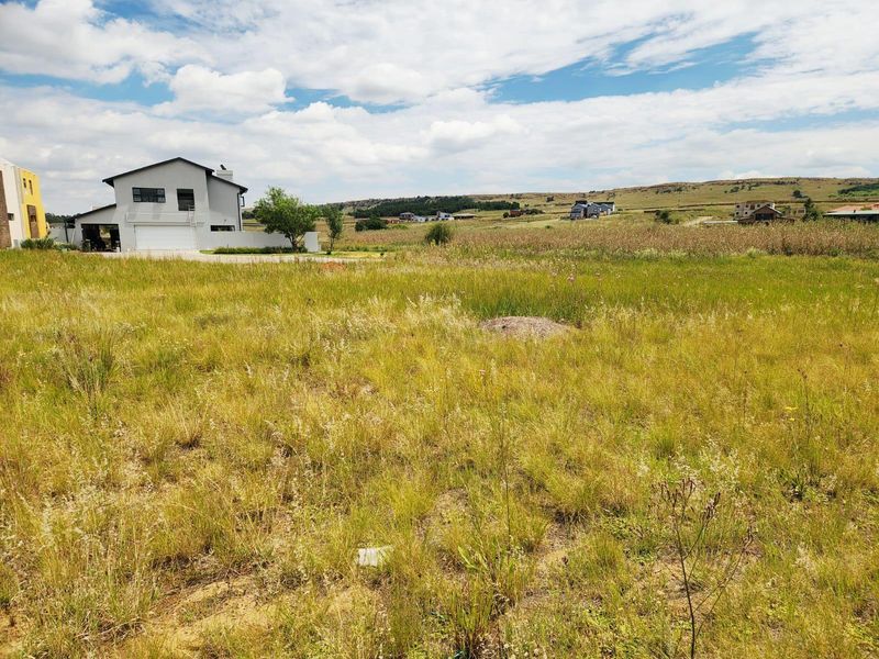 A vacant residential plot featuring natural grassland with surrounding neighborhood views and nearby established residential properties.