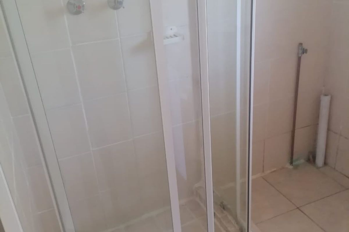 A bathroom featuring a corner shower enclosure with tiled walls and flooring, currently showing exposed plumbing and unfinished wall sections.