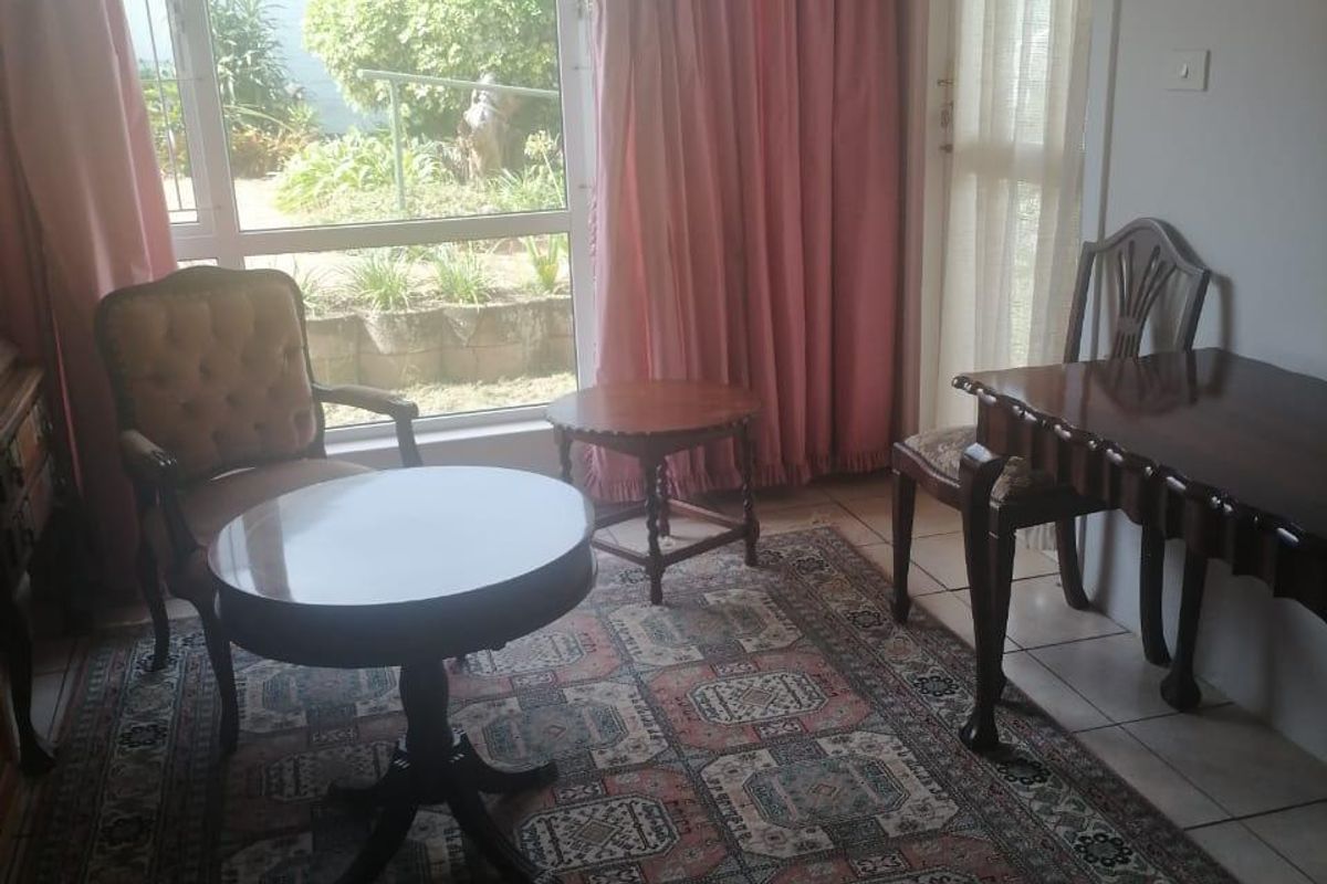 A living area featuring tiled flooring and large windows providing natural light and access to the garden.