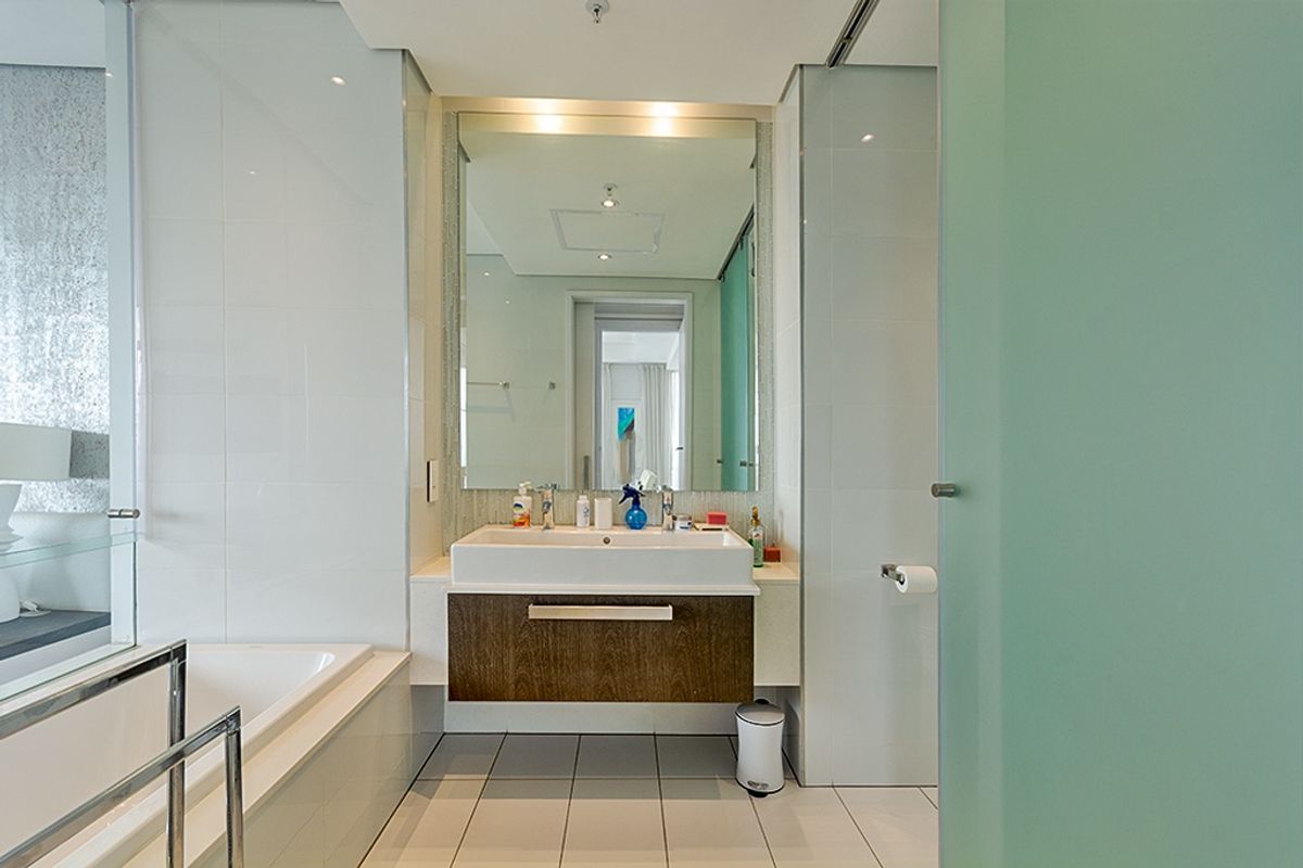 Modern bathroom featuring a built-in vanity, large wall-mounted mirror, tiled flooring, and a built-in bathtub with a frosted glass privacy door.