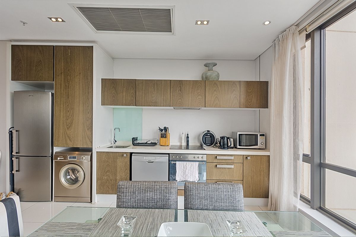 Modern kitchen featuring wood-grain cabinetry, integrated appliances, built-in oven, cooktop, and ducted air conditioning, finished with clean lines and neutral tiling.