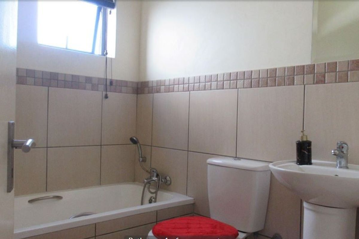 A functional bathroom featuring a bathtub with a handheld shower attachment, a pedestal basin, and a standard toilet with neutral wall tiling.