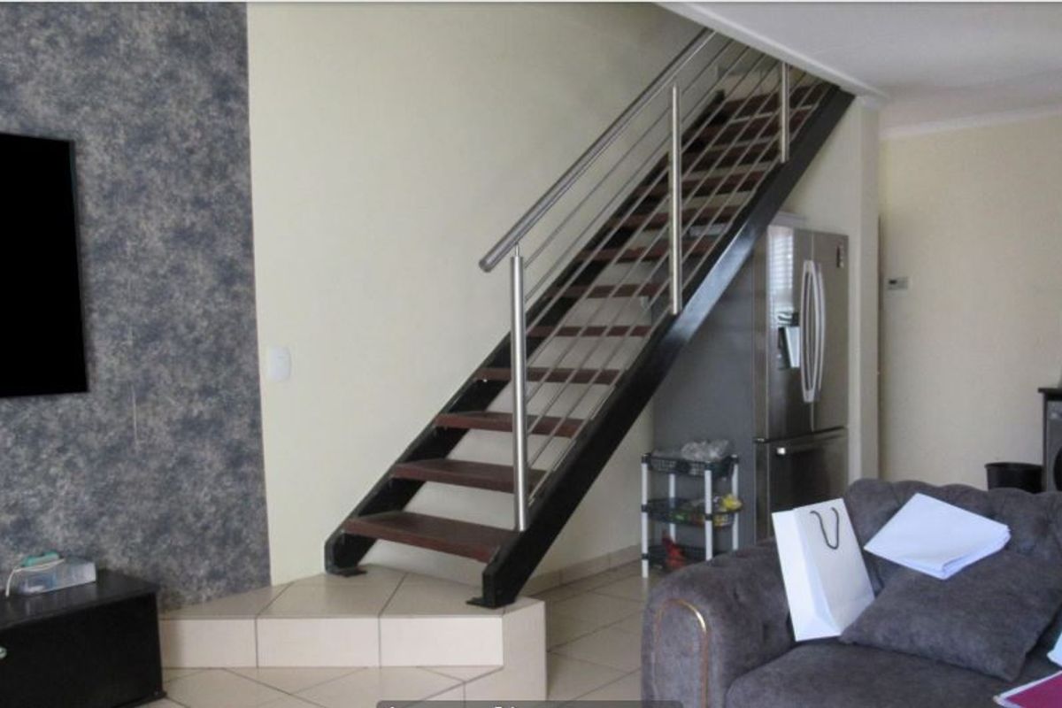 Living area featuring a modern staircase with stainless steel balustrades and a textured feature wall, providing a contemporary architectural element to the space.