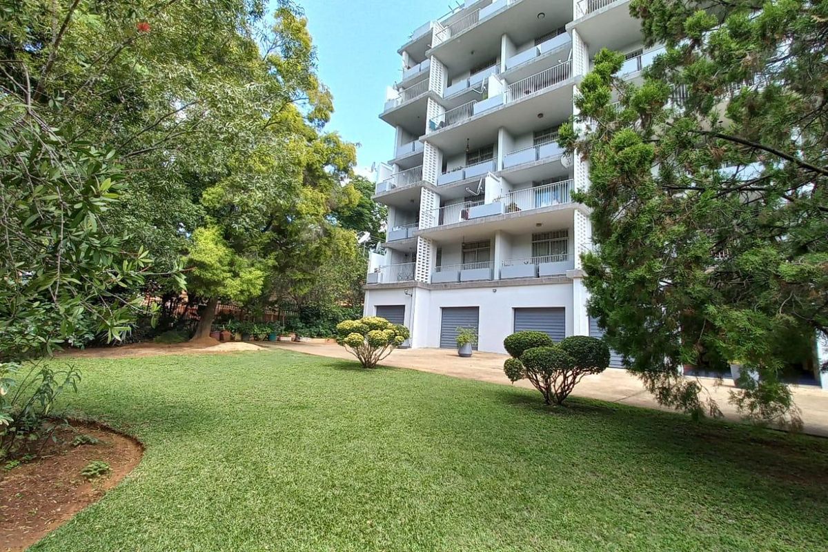 Exterior view of a multi-story apartment building featuring private balconies, ground-level garage access, and a well-maintained communal garden area.