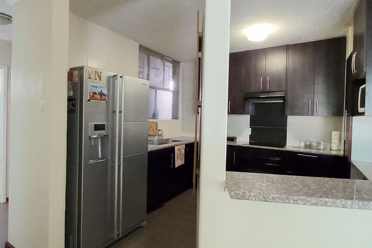 A functional kitchen featuring dark cabinetry, stone-look countertops, a built-in oven, and an extractor fan, with an adjacent hallway and breakfast bar.