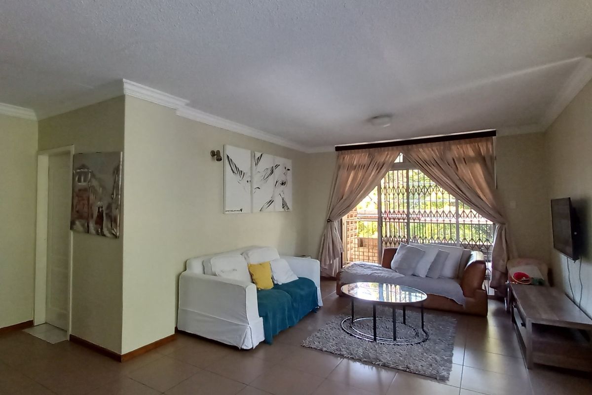 Spacious living room featuring tiled flooring, crown molding, and large windows with security gates, providing access to an outdoor balcony area.