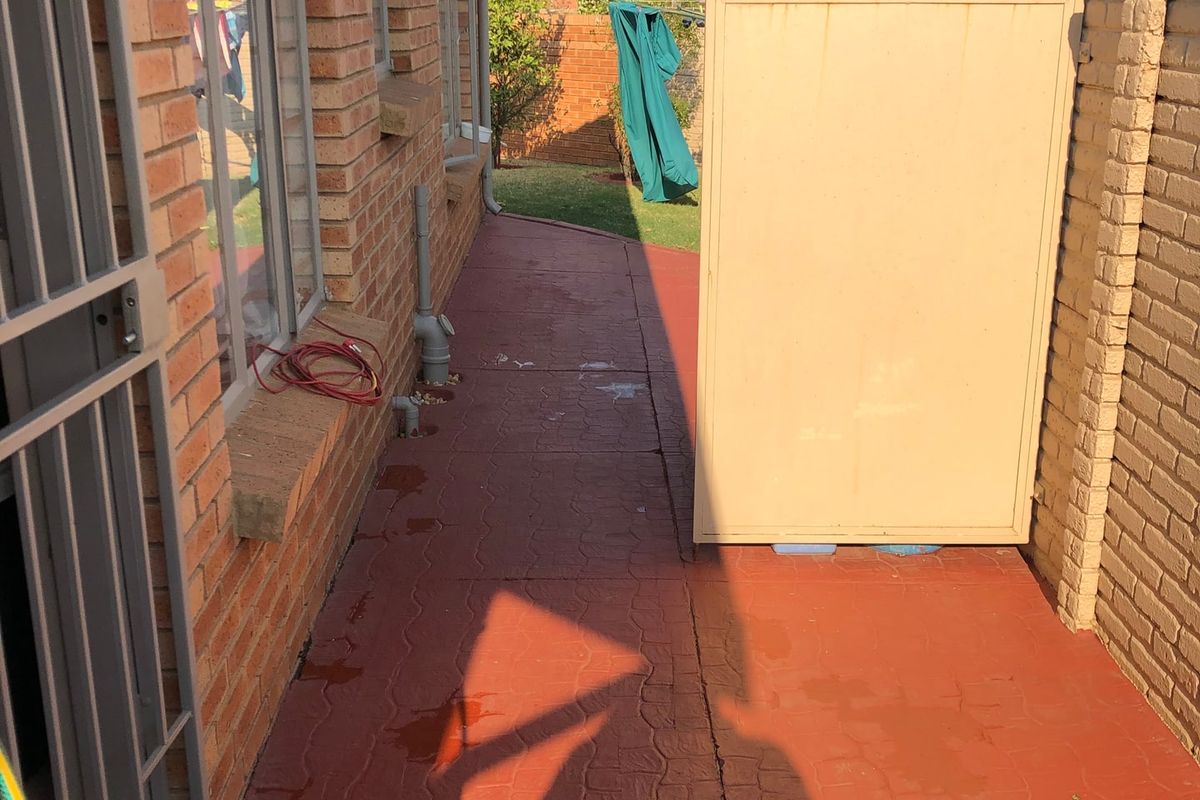 A side exterior walkway featuring face brick walls, paved flooring, and security gate access to the rear of the property.