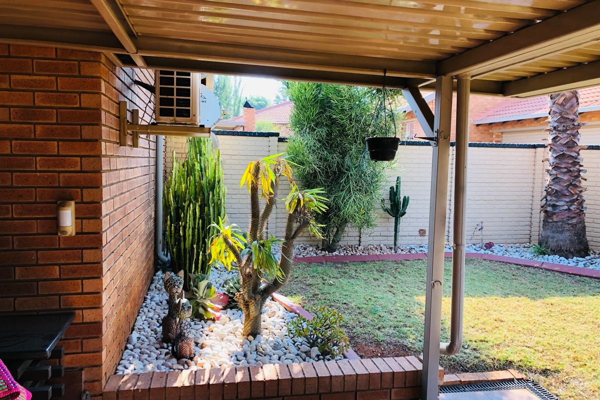 A covered outdoor patio area featuring brick wall construction, paved flooring, and a view of the landscaped garden with stone accents.