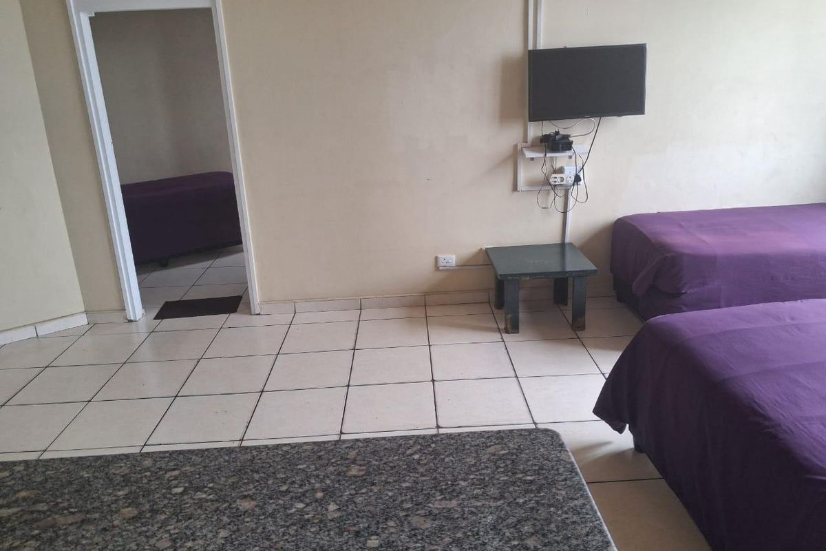 A bedroom featuring tiled flooring and wall-mounted television, showing signs of wear and requiring cosmetic updates to improve the overall aesthetic.