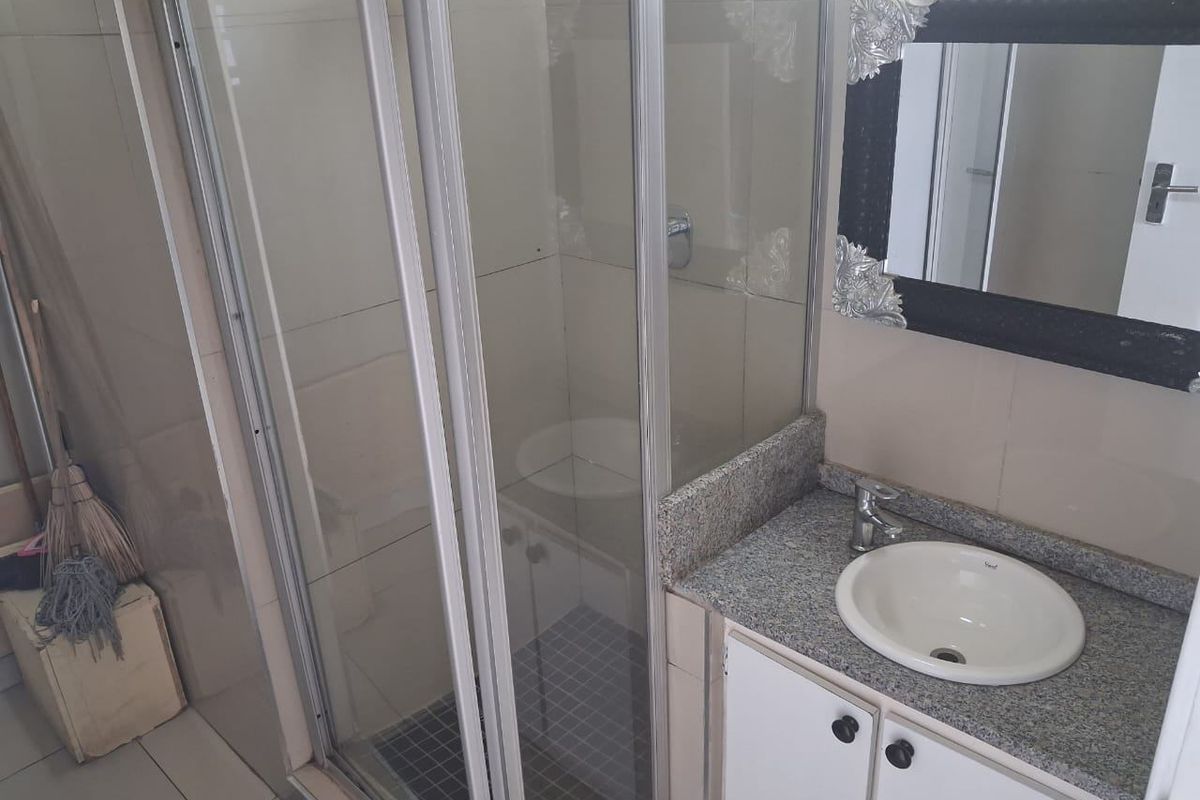 A functional bathroom featuring a glass shower enclosure, a granite-topped vanity with a drop-in basin, and neutral wall tiling.