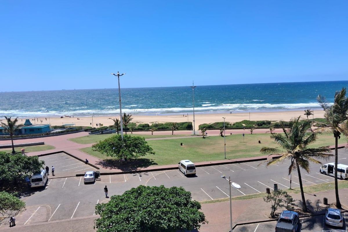 A clear, elevated view overlooking the beach, promenade, and public parking area, showcasing the coastal location and proximity to the ocean.