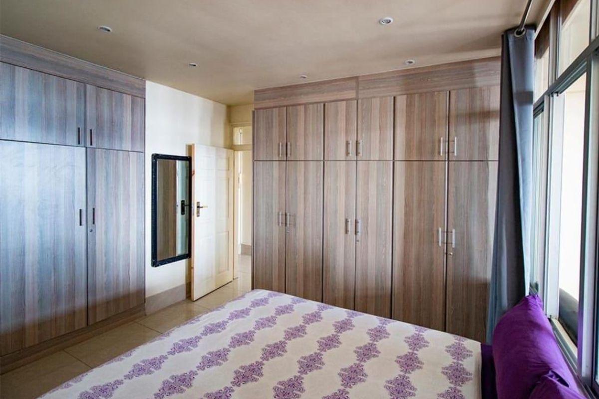 A well-maintained bedroom featuring extensive floor-to-ceiling built-in cupboards, recessed ceiling lighting, and neutral tiled flooring.